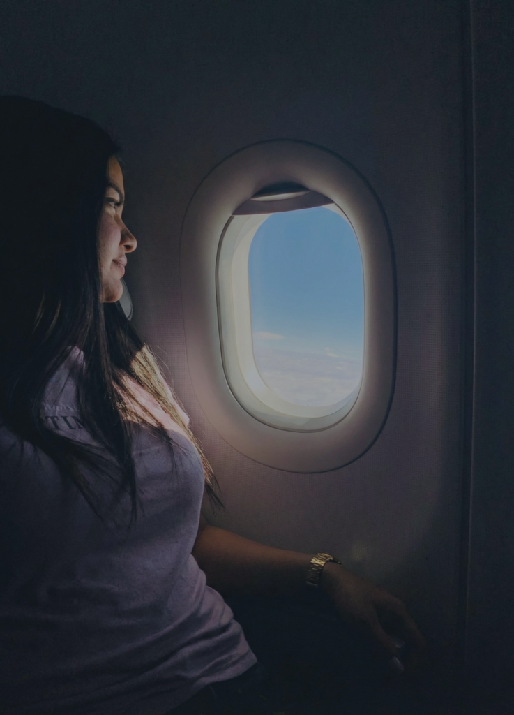Mujer migrante mirando por la ventana de un avión, representando los desafíos abordados en la Terapia Transpersonal en Línea